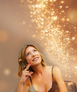 Smiling woman holding makeup brush surrounded by glowing particles