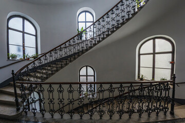 Interior photo of a historic staircase with arched windows and wrought iron railing. Detail of...