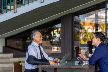 Senior manager with broken elbow works together with young manager to exchange ideas for an...