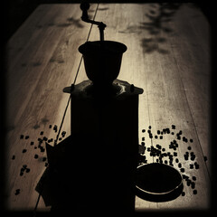 Dramatic silhouette of a vintage coffee grinder and coffee beans on a rustic wooden table,...