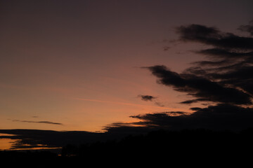 nuvole scure in primo piano, in controluce, nel cielo arancione e viola, al tramonto