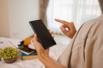 Asian woman hands using white smartphone with blank screen while lying in bed at morning
