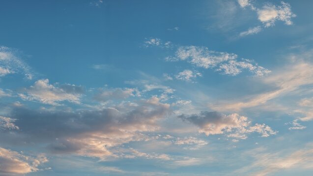 Blue sky with scattered wispy clouds soft golden sunlight pastel tones high altitude cirrus and altocumulus layers gentle evening atmosphere serene open expanse