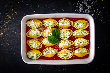 Pasta shells stuffed with cheese and spinach in tomato sauce in baking dish prepared for baking on black table
