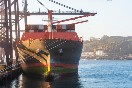 Cargo container ship under gantry cranes in the San Antonio port, Chile. She is loaded with cargo in the containers.