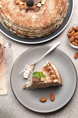 Piece of tasty crepe cake with cocoa powder, chocolate and nuts served on light table, flat lay