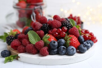 Different ripe berries and mint leaves on white tiled table, closeup