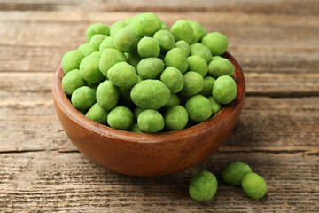 Delicious wasabi coated peanuts in bowl on wooden table, closeup