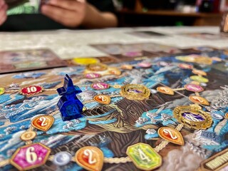 A close-up of a tabletop game figure on the board, with friends gathered around the table, as a...