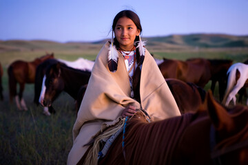 A young native american girl dressed in traditional clothing sits on a horse surrounded by other horses as the sun sets, creating a serene atmosphere in the countryside. Generative AI.