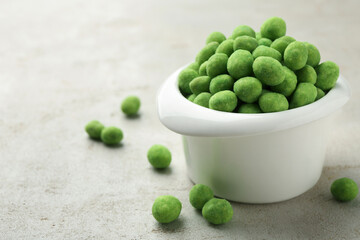 Wasabi coated peanuts in bowl on light table, closeup. Space for text
