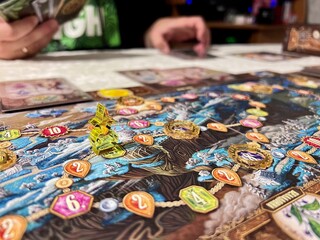 A close-up of a tabletop game figure on the board, with friends gathered around the table, as a background.