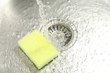 Water going down drain and sponge in sink, closeup