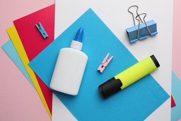Glue in bottle, color paper and other stationery on pink background, flat lay