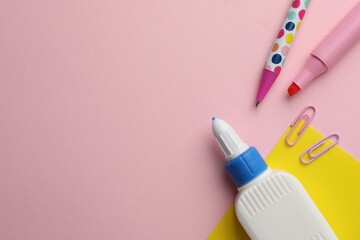 Glue in bottle, felt pen and paper clips on pink background, flat lay. Space for text