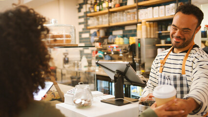 Man With Down Syndrome Serving Female Customer At Coffee Shop Checkout