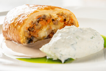 Gourmet savory pastry with vegetable filling, plated with creamy mousse, green and beige sauces, and herb garnish. Elegant restaurant-style presentation, close-up view
