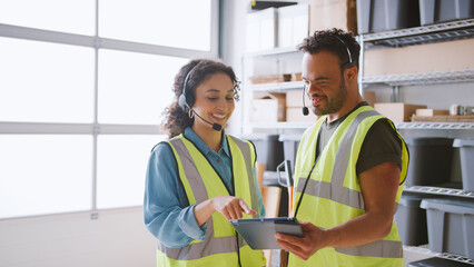 Man With Down Syndrome Using Digital Tablet With Female Colleague In Warehouse Wearing Headsets © Monkey Business