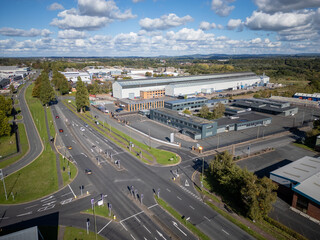 Modern warehouse and distribution depot seen from above with metal cladding, parking bays and surrounding trees in industrial estate on bright sunny day