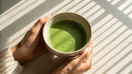 A person is drinking hot matcha tea from a cup, perhaps during a morning break