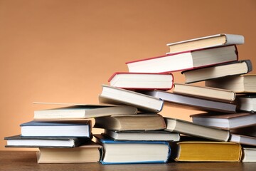 Group of different stacked books on wooden table against light brown background