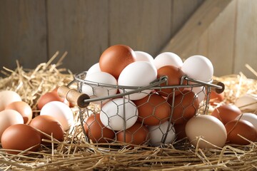 Raw chicken eggs in metal basket on straw, closeup