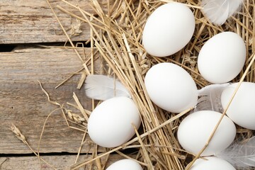 Raw chicken eggs, feathers and straw on wooden table, flat lay. Space for text