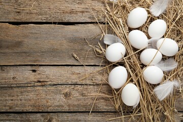 Raw chicken eggs, feathers and straw on wooden table, flat lay. Space for text