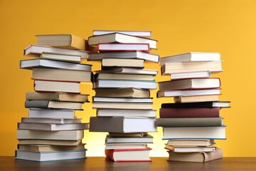 Many stacked books on table against yellow background