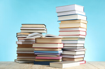 Many stacked books on wooden table against light blue background