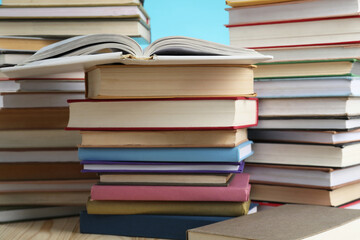 Many stacked books on wooden table against light blue background, closeup