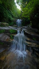 A beautiful cascading waterfall flows over mosscovered rocks in a lush green forest, creating a serene natural landscape