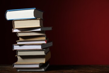 Many stacked books on table against red background. Space for text