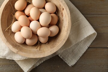Raw chicken eggs and straw in bowl on wooden table, top view. Space for text