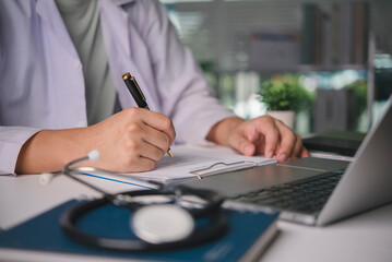 Physician writing a prescription on a form at a clinic desk, close-up of hand with pen, documenting patient information, medical history for professional healthcare service, with stethoscope nearby.