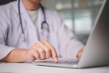 Close up of doctor hand using laptop touchpad, working on electronic health records EHR in a hospital office, representing telemedicine, digital healthcare technology, and patient data management.