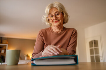 Low angle view of pensive old woman with hands on photo album thinking of past family memories at home
