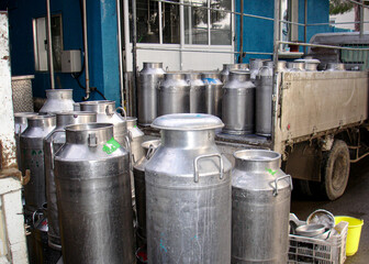 Large, shiny aluminum milk cans stacked on back of small truck, loading dock of dairy, milk processing plant. typical scene illustrating logistics of milk collection and food industry supply chain.