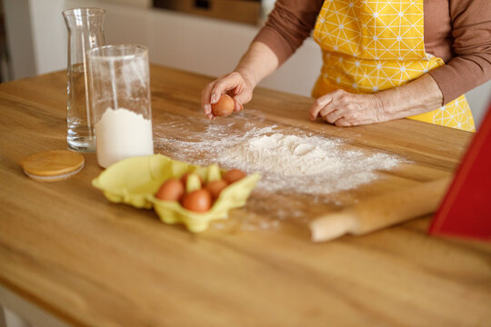 Midsection of senior woman cracking eggs into flour on kitchen island while preparing cookies at home