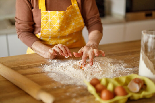Midsection of elderly woman in apron mixing egg in flour while preparing content for food blog at home