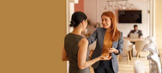 Female professionals brainstorming ideas and working together while standing by wall in corporate office