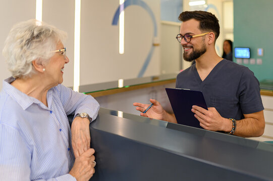 Young male doctor explaining medical procedure to elderly woman at reception counter during hospital visit