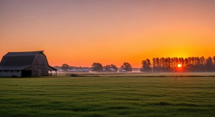 Peaceful rural farmland at sunrise with traditional barn and outbuildings silhouetted against vibrant orange sky. Morning mist drifts across green pastures while sun emerges through tree line.