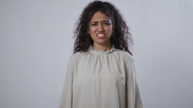 A young South Asian woman with curly brown hair is clenching her teeth and looking angry or frustrated
