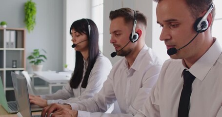 Each operator in a bright office answers inquiries on a laptop, speaking through a headset and offering friendly customer service via the hotline. Team with headsets provides customer support.