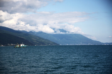 view of mountains hidden by clouds on the sea coast and floating boat