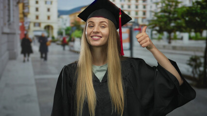 Woman in graduation uniform standing on city street showing thumbs up and thumbs down with...