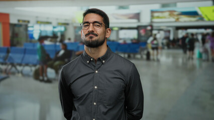 Obraz premium Young man standing confidently in a busy airport terminal with travelers in the background indicating an international travel setting.