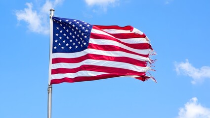 Obraz premium Tattered american flag waving in clear blue sky