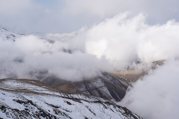 Dramatic high mountain landscape with snow, rocks and low clouds